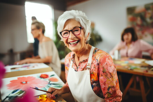 Portrait of smiling senior woman painting picture with her friends in background