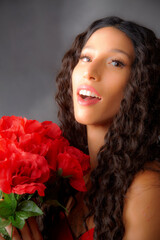 Naklejka premium Glamourous studio portrait of young Latina woman holding red flowers.
