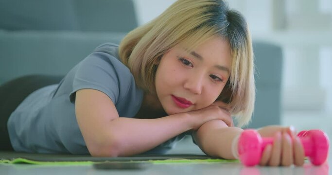 Engaged in her home workout, a young Asian woman battles moments of boredom and laziness while trying to exercise independently at her residence.