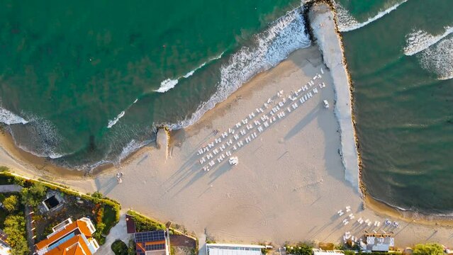 Drone top-down view of sea waves and sandy beach with sunbeds at Robinson Beach on the Bulgarian Black Sea coast