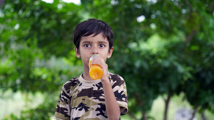 Fototapeta premium Happy Cute Indian boy drinking juice in the park, holding plastic bottle and showing thumb up. outdoor shot