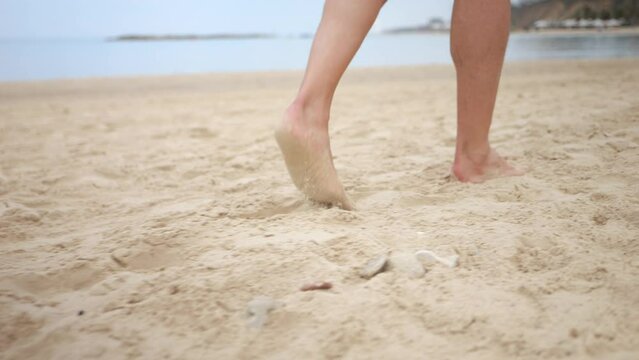 Tracking handheld shot of person’s legs and barefeet walking across sandy beach