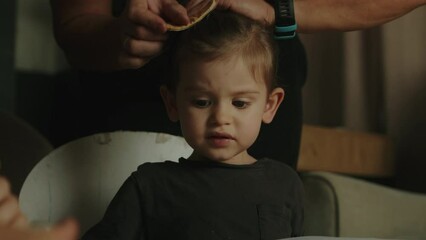 Father hands styling daughter's hair while sitting at table, expressing positive emotions. Morning routine concept.