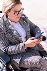 businesswoman using wheelchair using mobile phone outdoors at the financial district, concept of...