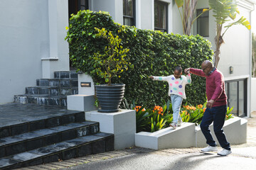 Happy african american grandfather and granddaughter walking in front of house, copy space