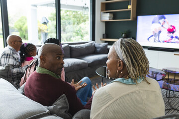 Excited african american parents, son, daughter and grandparents watching rugby on tv, slow motion