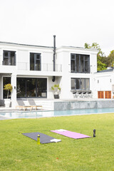 General view of house with terrace, swimming pool and yoga mats in sunny garden, copy space