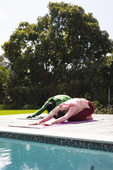 Diverse couple practicing yoga stretching next to swimming pool in sunny garden, copy space