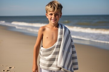 Portrait of smiling boy wrapped in towel standing on beach and looking at camera - Powered by Adobe