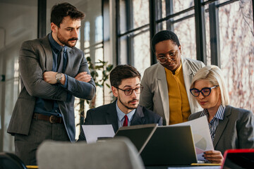 A multi-ethnic group of coworkers in a conference room, sitting around laptops, brainstorming and strategizing for success