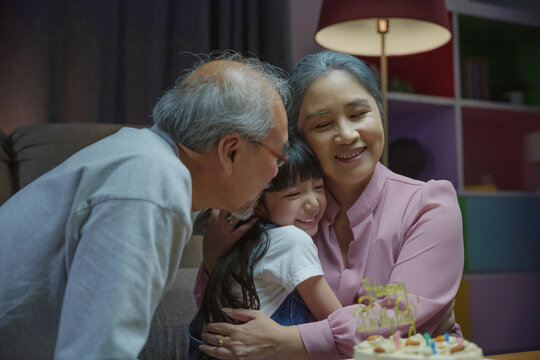 Happy Birthday. Family grandfather and grandmother hugging granddaughter feeling thankful while celebrating his birthday after giving wonderful cake, Asian senior family party with kid at home