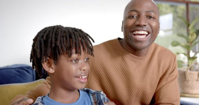 Portrait of happy african american father and son embracing on sofa at home, slow motion