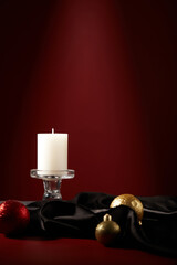 White scented candle arranged over red background with blinking baubles and a black fabric. A...