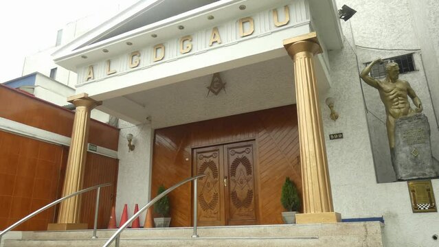 A Masonic lodge. Two golden pillars on each side. On the top the acronym which reads ALGDGADU. Large wooden doors to the temple and above the masonic G. Located in Lima, Peru.