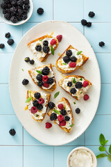 Toasted bread with ricotta, blackberries and raspberries. Breakfast concept. Tiled background. Top view.