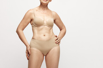 Cropped image of female body in underwear against grey studio background. Elegant senior woman with...
