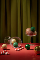 Transparent glasses containing pastel color baubles decorated with few candy cane on red surface....