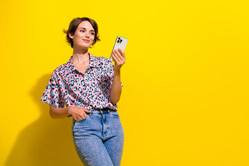 Portrait of lovely positive person use smart phone texting empty space ad isolated on yellow color background