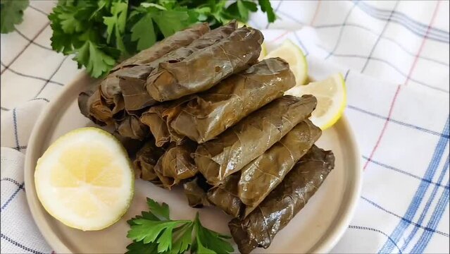 Traditional oriental Turkish dolma made of grape leaves stuffed with rice and meat lies on a plate with parsley and lemon slices