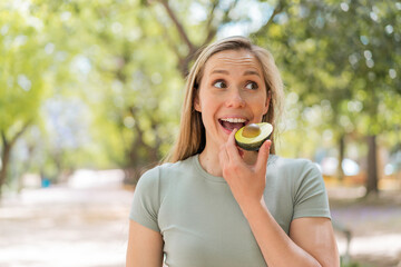 Fototapeta premium Young blonde woman at outdoors holding an avocado
