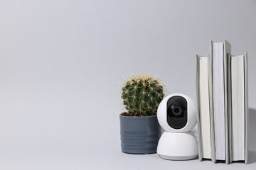 Home security camera, cactus and books on gray background, space for text
