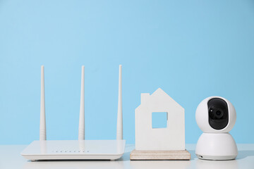 Wooden house, router and security camera on blue background