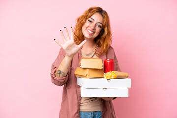 Young caucasian woman holding fast food isolated on pink background counting five with fingers