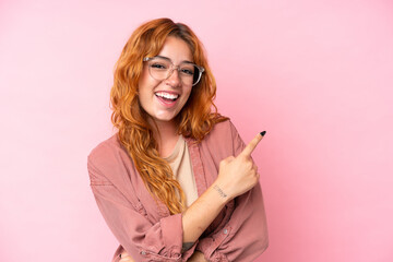 Young caucasian woman isolated on pink background With glasses and pointing side