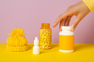 Jars with pills, liquid bottle, yellow cap and female hand on pink background
