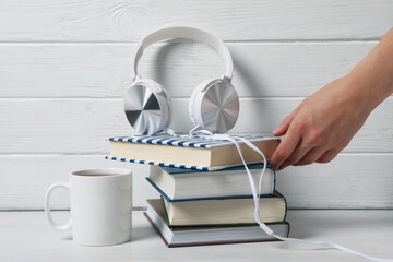 Stack of books, headphones, cup of tea and hand on white wooden background