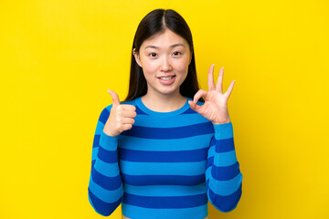 Young Chinese woman isolated on yellow background showing ok sign and thumb up gesture