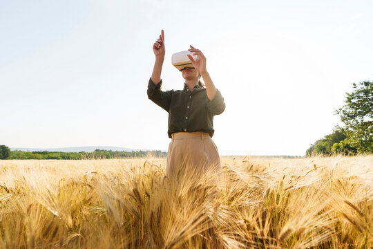 Businesswoman using virtual reality simulator standing amidst crops - Powered by Adobe