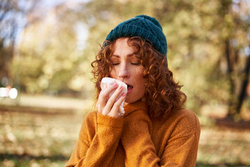 Redhead woman sneezing at autumn park