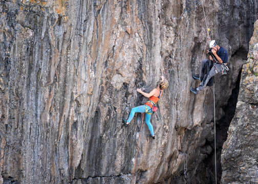 Man photographing woman climbing mountain with rope