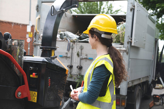 Blue collar worker looking at dumper truck picking up garbage
