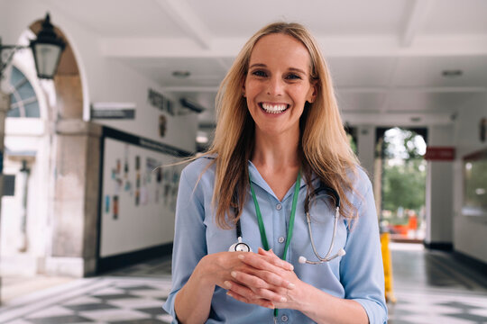 Cheerful doctor standing with hands clasped at hospital