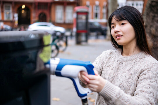 Young woman holding electric plug at vehicle charging station