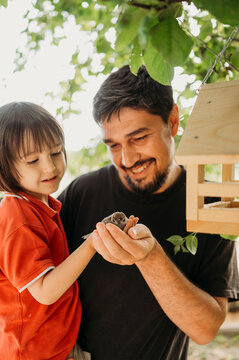 Smiling father and son holding sparrow near bird house