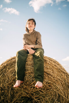 Boy sitting on haystack with sky in background