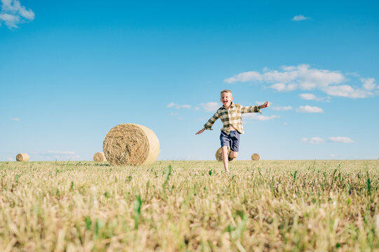 Happy boy running in field with haystacks