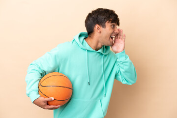 Handsome young basketball player man isolated on ocher background shouting with mouth wide open to...