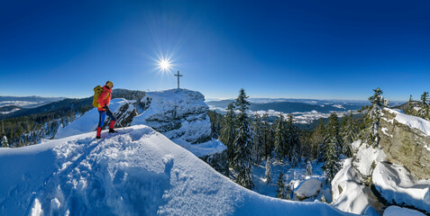 Woman in ski-wear hiking near summit cross on snowcapped mountain