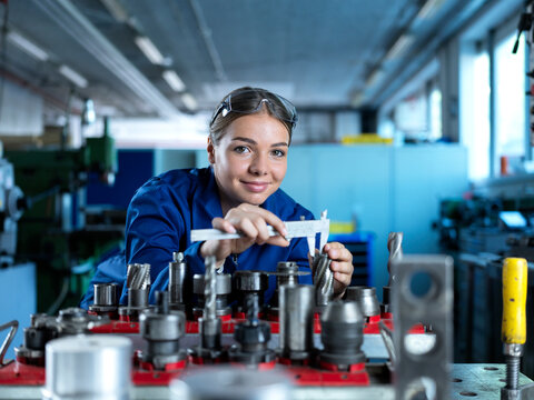 Smiling metal worker measuring CNC machine with caliper at manufacturing factory