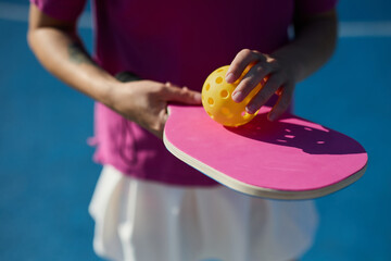 Female pickler holding a pickleball racket and perforated plastic ball in hands on court
