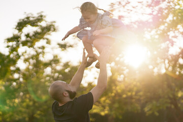 young father throwing his daughter in the air on a summer day in park, happy moments in life - obrazy, fototapety, plakaty