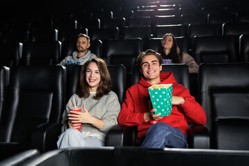 A beautiful smiling couple is watching a movie at the cinema and eating popcorn