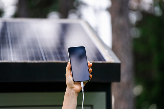 Hand of woman holding smart phone with solar panel in background