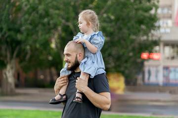 young dad holding his little daughter on his shoulders outdoors, having fun, happy moments