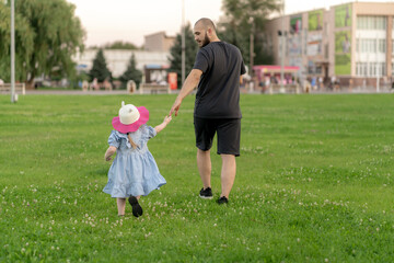 view from behind of a father walking with his child outdoors, holding his hand