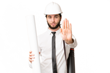 Young architect man with helmet and holding blueprints over isolated chroma key background making stop gesture